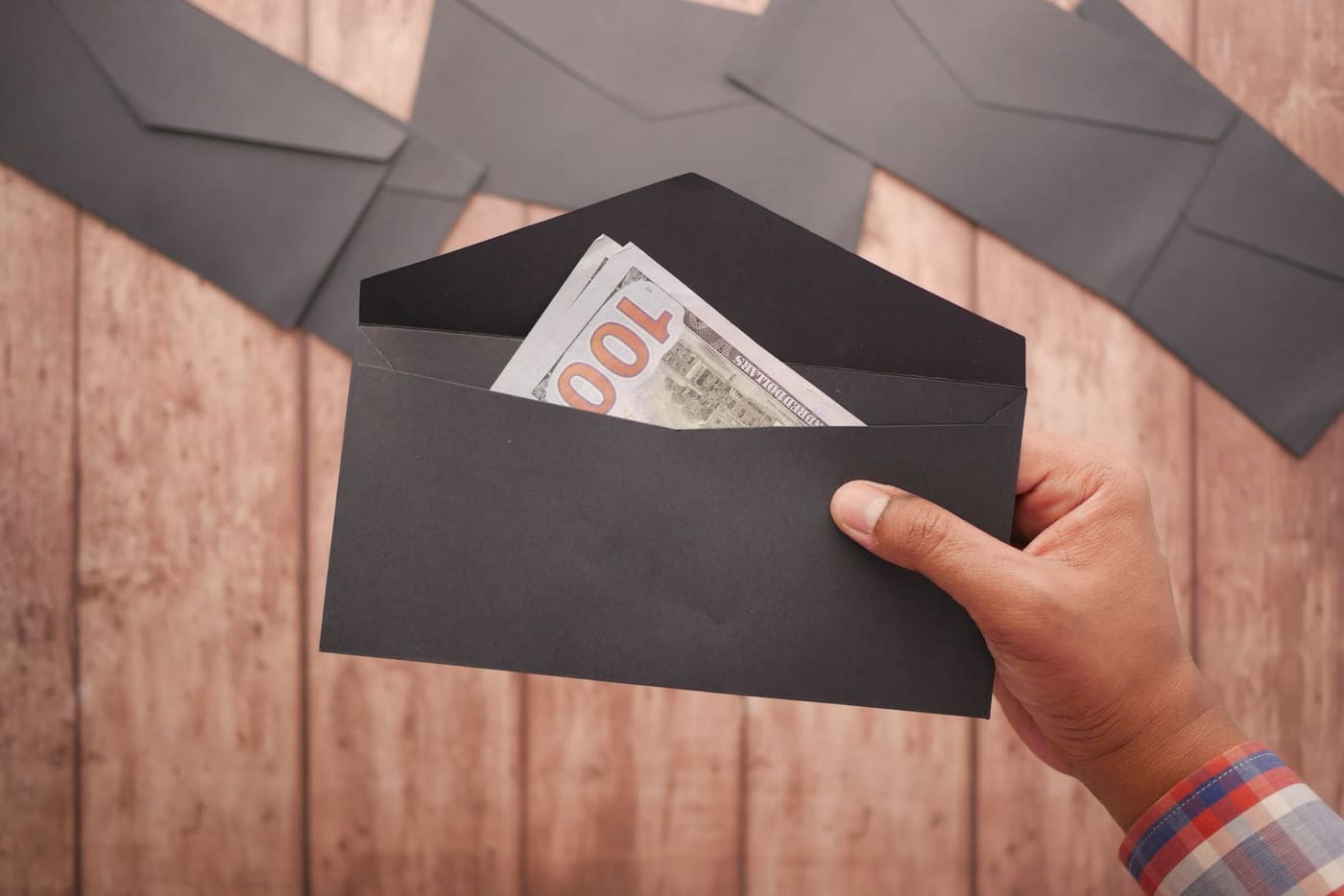 A hand holding a black envelope with a bill tucked inside, on a wooden surface