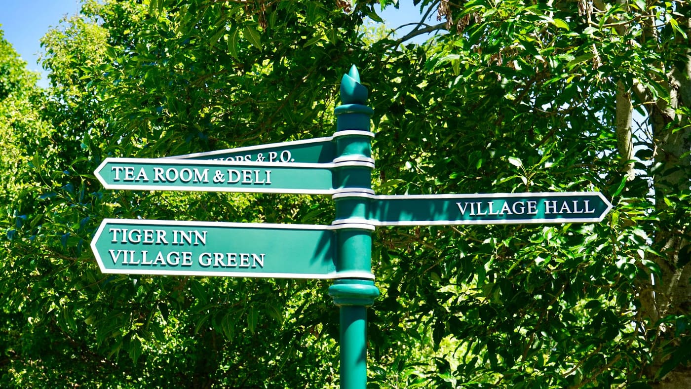 A green village signpost with several direction arms among trees