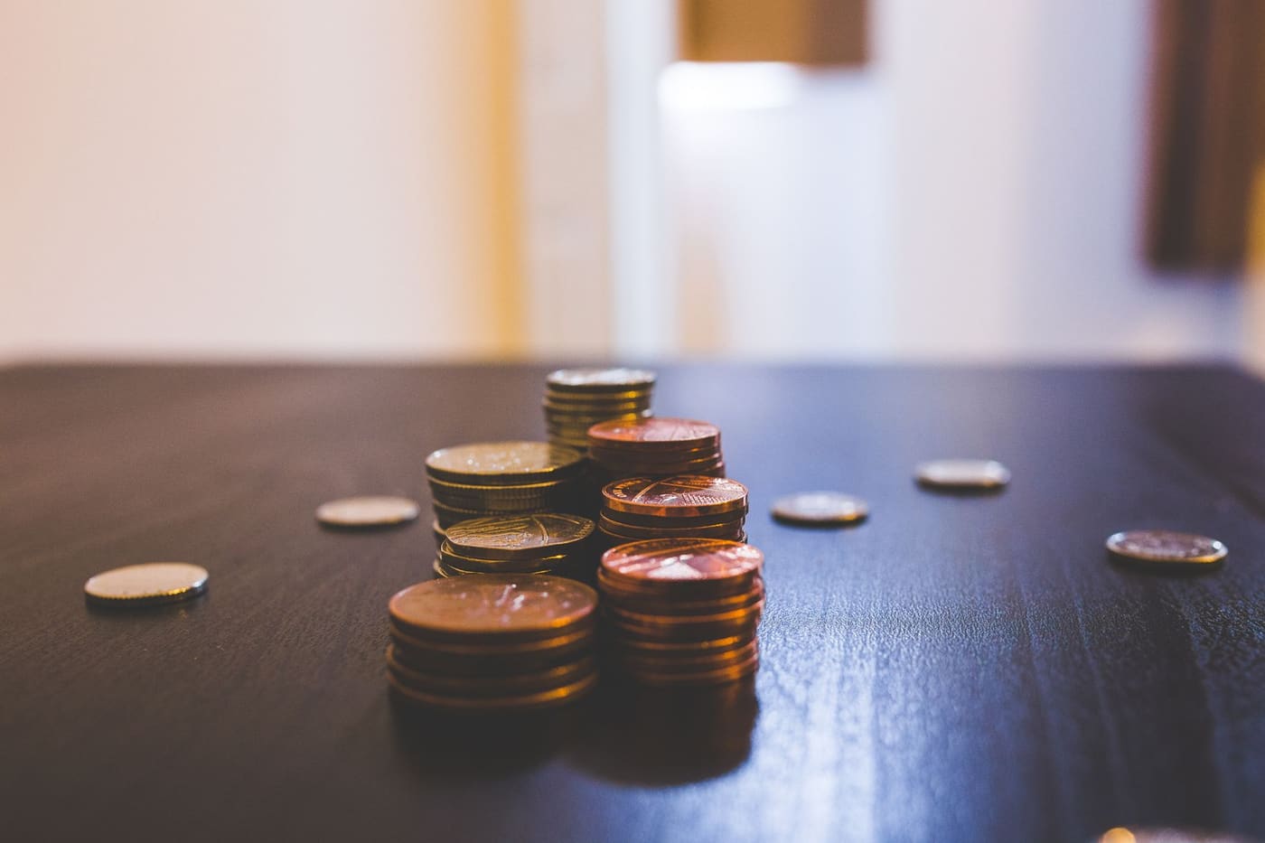 A small stack of coins and a few loose coins on a dark table