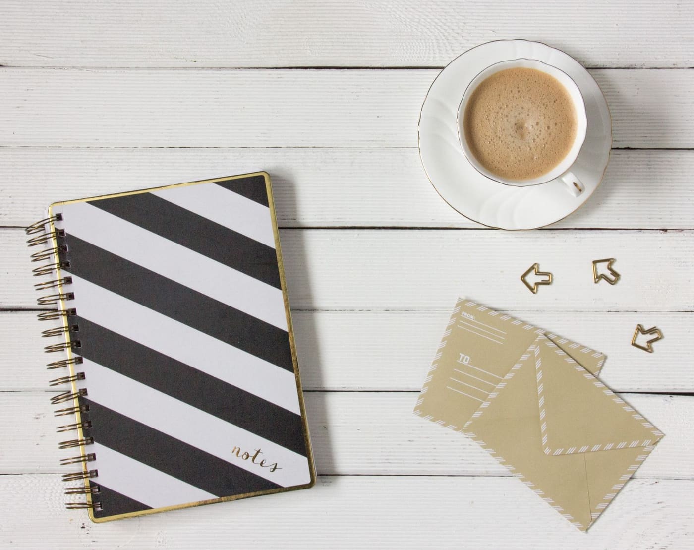 Striped notebook, a cup of coffee and envelopes on a white wooden table